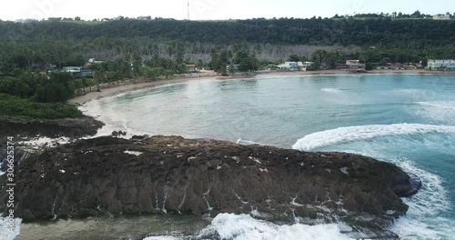 Aerial shot of beach rock and waves crashing in Jobos Puerto Rico with town in background photo