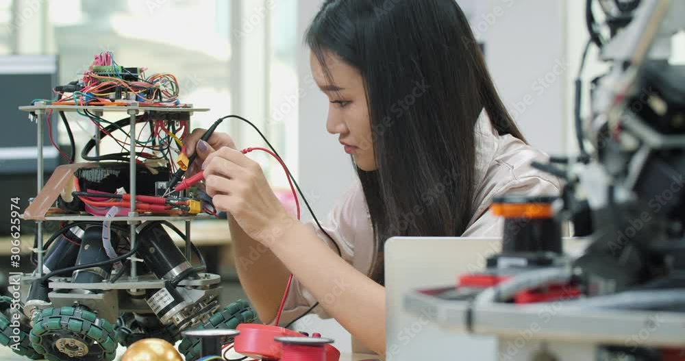 Asian teenage engineer assembling and testing robotics responses in laboratory. Architects design circuit meeting share technology ideas and collaborating development robot.