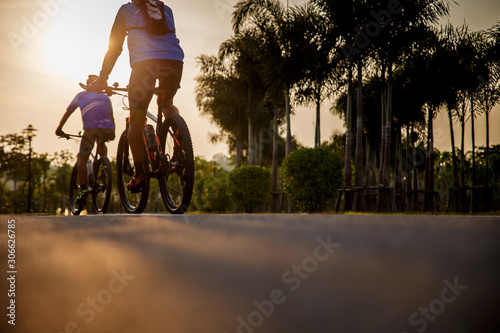 Two preson ride on bike on the road. Sport and active life concept sunset time. Couple of men riding on bicycle in a park. Blue sky with orange sun beam over the body of cyclist.