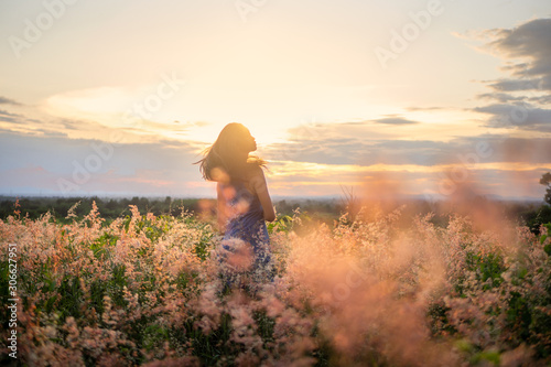 Trendy girl in stylish summer dress feeling free in the field with flowers in sunshine.