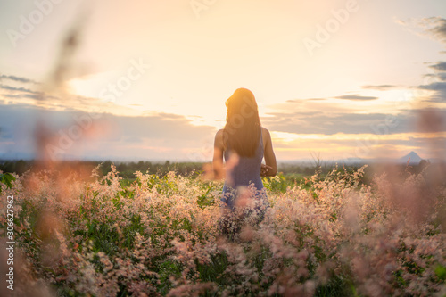 Trendy girl in stylish summer dress feeling free in the field with flowers in sunshine.