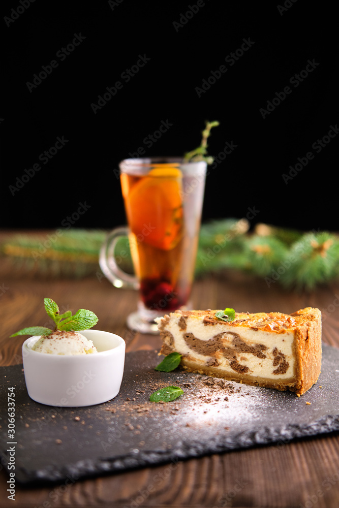 Layered cheesecake with ice cream and fruit tea served on slate plate on dark wooden background