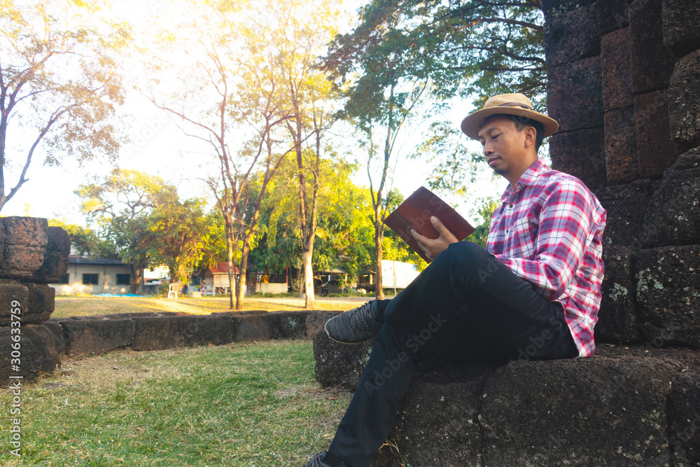 Fototapeta premium Asian man sitting and reading book in old stone temple,he is reading book and relaxing time. learning day,clever,intelligent,Photo vacations and Lifestyle concept idea.