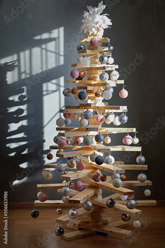 eco-friendly creative Christmas tree made of boards. alternative Christmas tree decorated with toys for the new year . in a dark room, in the light from the window .