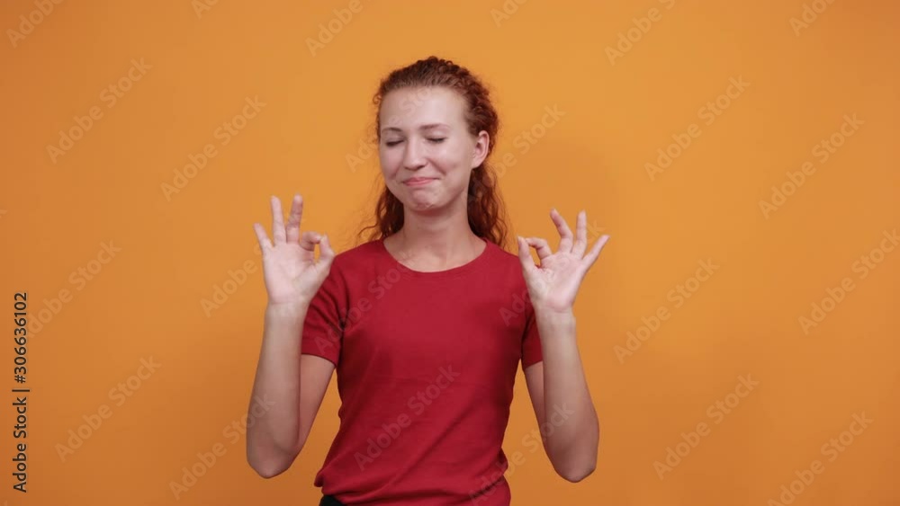 Attractive young lady in red shirt showing okay gesture, smiling isolated on orange background in studio. People sincere emotions, health concept. Attractive young lady in red shirt showing okay gesture, smiling isolated on orange background in studio. People sincere emotions, health concept.