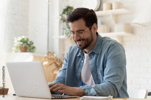 Smiling young man using laptop studying working online at home