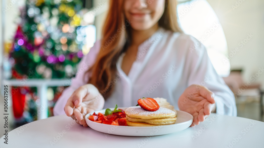 A woman holding and showing a plate of pancakes with strawberries and whipped cream