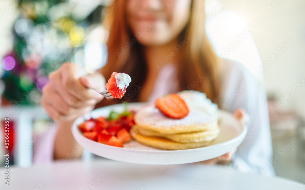 A woman holding and eating pancakes with strawberries and whipped cream by fork