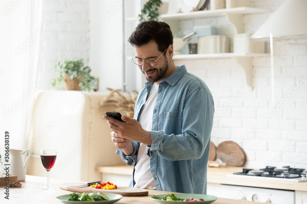 Happy young man preparing romantic dinner using smartphone app Happy young man preparing romantic dinner using smartphone app