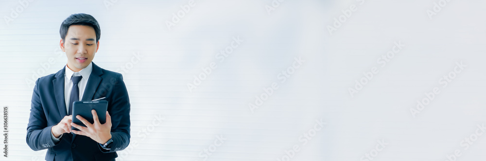 young businessman Asian wear a black suit, and standing smart poses. hold a digital tablet and use it. on a white background.with banner copy space young businessman Asian wear a black suit, and standing smart poses. hold a digital tablet and use it. on a white background.with banner copy space