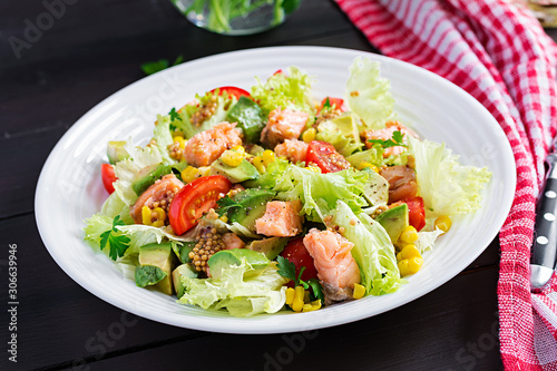 Salad with grilled salmon, lettuce, avocado, tomatoes and corn on a white bowl. Paleo diet.