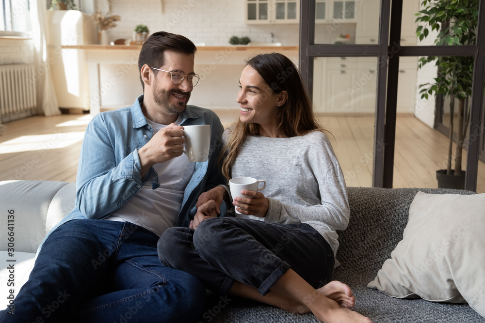 Happy young couple relaxing on sofa talking drinking tea Happy young couple relaxing on sofa talking drinking tea