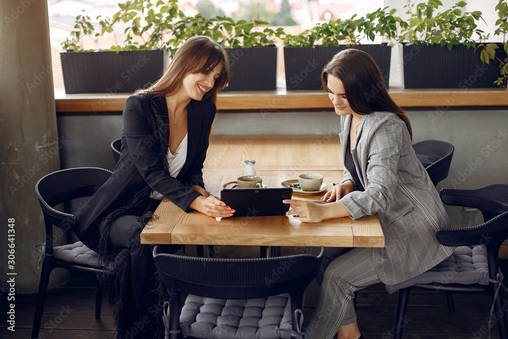 Fototapeta premium Two beautiful women working. Friends in a cafe. Businesswomen talking and working with a tablet