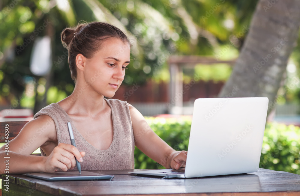 Young beautiful girl freelancer draws with a graphic tablet on the background of palm trees Young beautiful girl freelancer draws with a graphic tablet on the background of palm trees