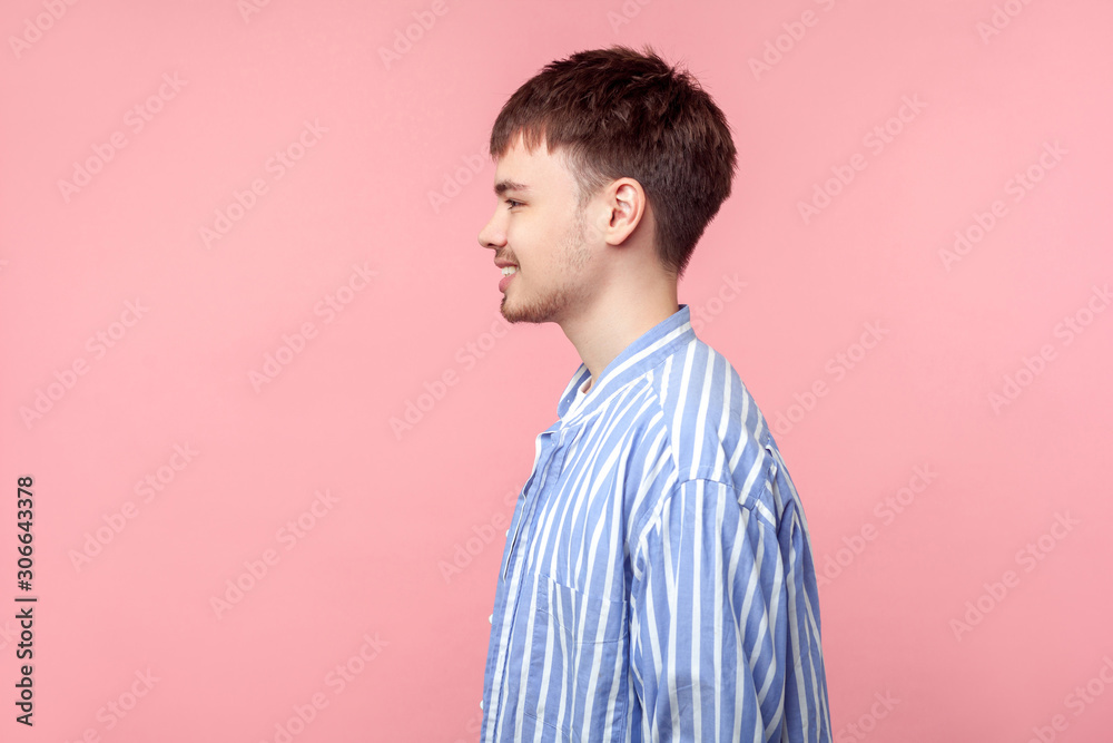 Side view portrait of positive brown-haired man with small beard and mustache in casual striped shirt, looking aside with toothy smile, optimistic view. indoor studio shot isolated on pink background Side view portrait of positive brown-haired man with small beard and mustache in casual striped shirt, looking aside with toothy smile, optimistic view. indoor studio shot isolated on pink background