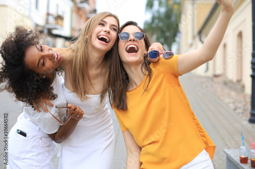 Three cute young girls friends having fun together, taking a selfie at the city.