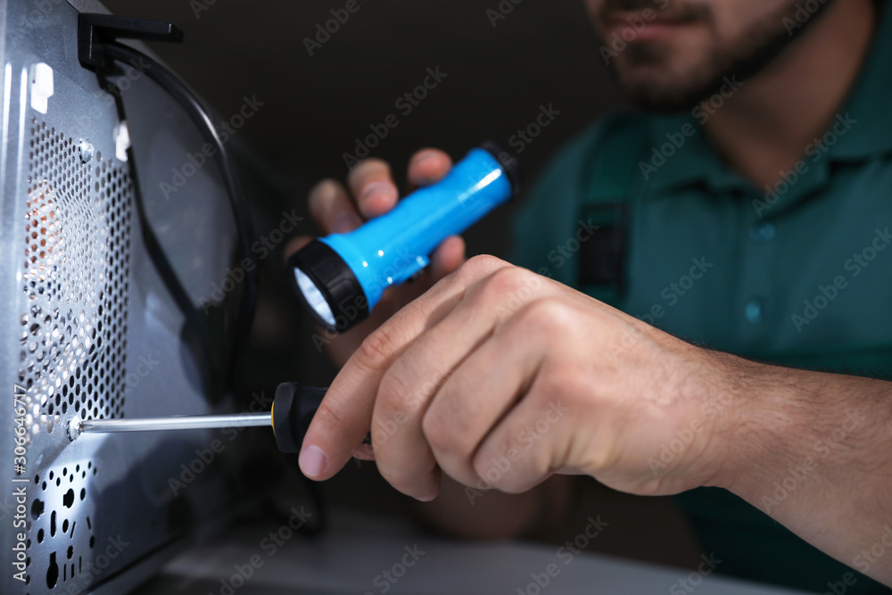 Repairman with flashlight fixing microwave oven indoors, closeup