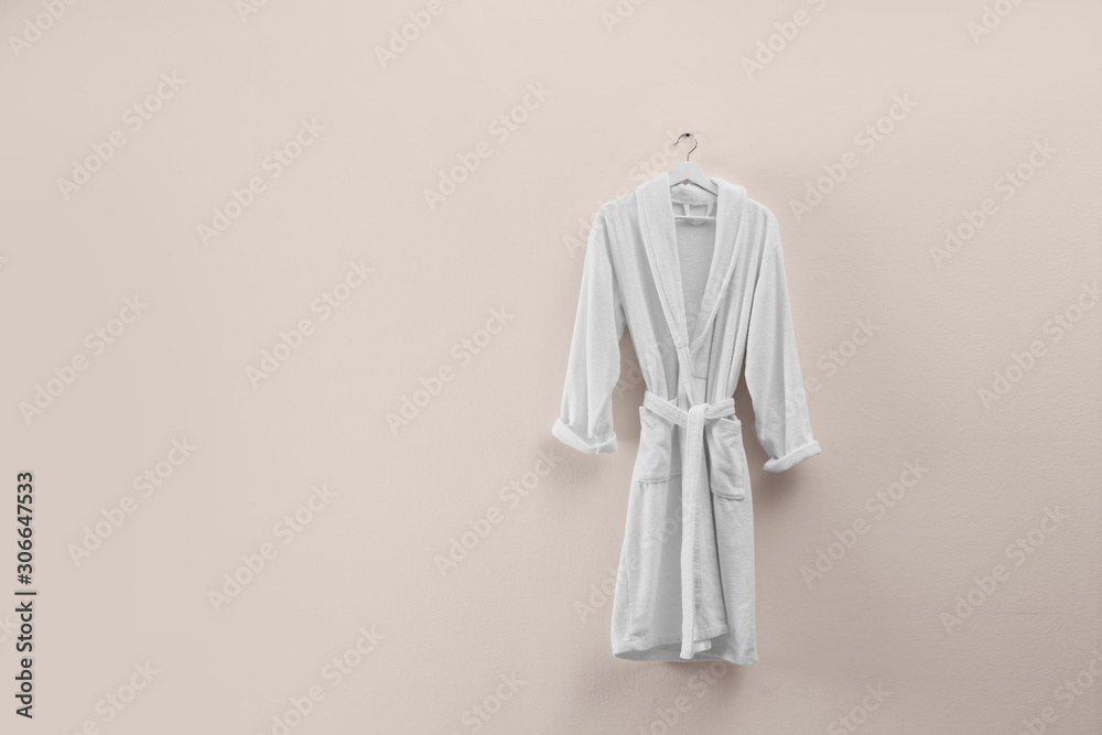 Soft comfortable bathrobe hanging on beige wall, space for text Soft comfortable bathrobe hanging on beige wall, space for text
