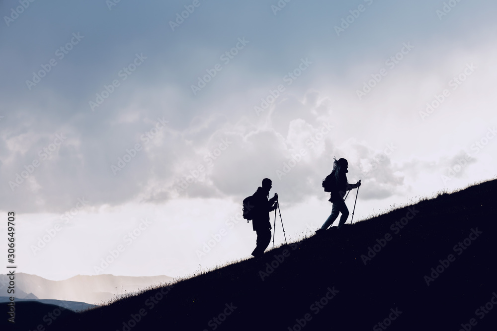 Two hikers silhouettes goes uphill in mountains