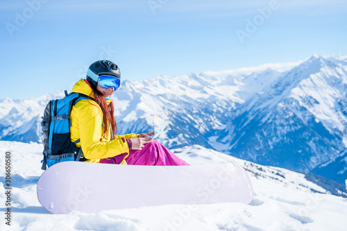 Photo of snowboarder girl in helmet with map in her hands sitting on mountain slope