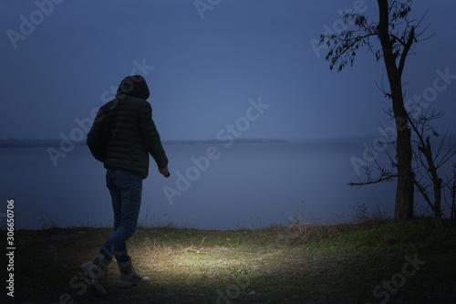 Man with flashlight walking near river in evening