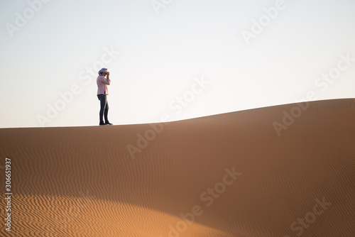 Woman with turban photographing the dune landscape in the Sahara desert.