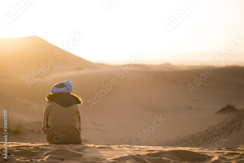 Berber with turban watching the sunset in the dune landscape in the Sahara desert.