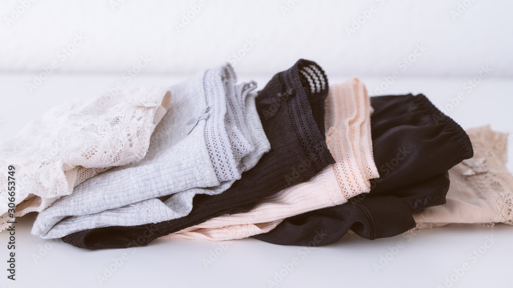 Stack of different women's panties lying on a white table in beige natural colour. Women underwear background. Copy space - obrazy, fototapety, plakaty 