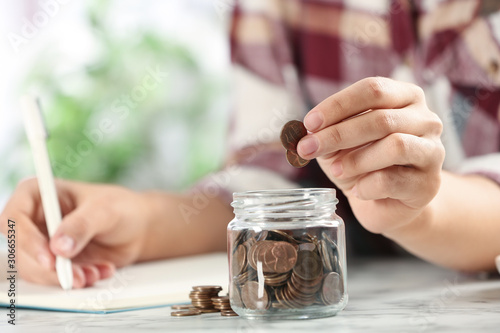 Woman putting money into glass jar at white marble table, closeup
