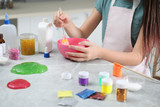 Little girl mixing ingredients with silicone spatula at table in kitchen, closeup. DIY slime toy