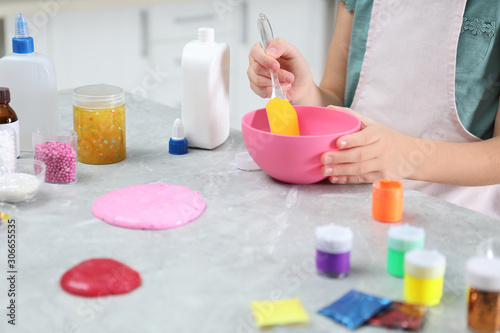 Little girl mixing ingredients with silicone spatula at table  closeup. DIY slime toy