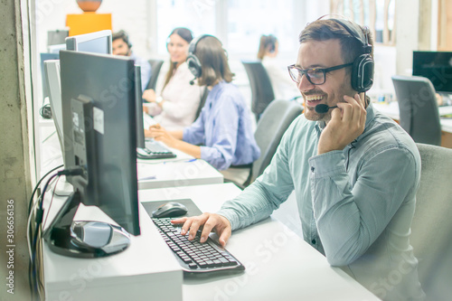 Smiling male call centre agent with headset working on computer in office