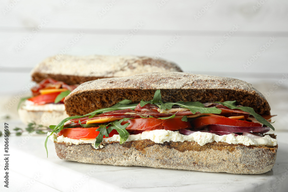 Delicious sandwiches with fresh vegetables and prosciutto on white table, closeup Delicious sandwiches with fresh vegetables and prosciutto on white table, closeup