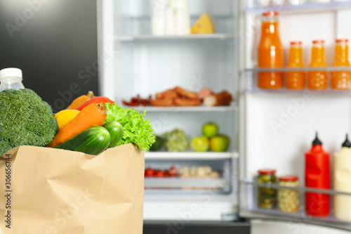Paper bag full of products near refrigerator, closeup