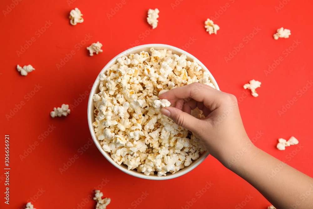 Woman taking fresh pop corn from bucket on red background, top view Woman taking fresh pop corn from bucket on red background, top view