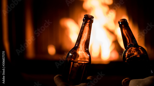 Two men drinking beer by the fireplace - hands with bottles on a background of burning fire