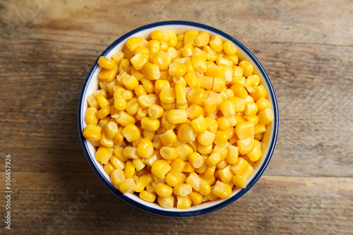 Delicious canned corn in bowl on wooden table, top view