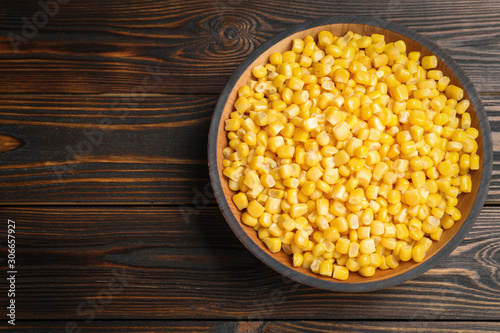 Delicious canned corn in bowl on wooden table, top view. Space for text