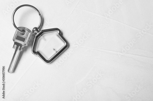 Key with trinket in shape of house on light grey stone background, top view and space for text. Real estate agent services © New Africa