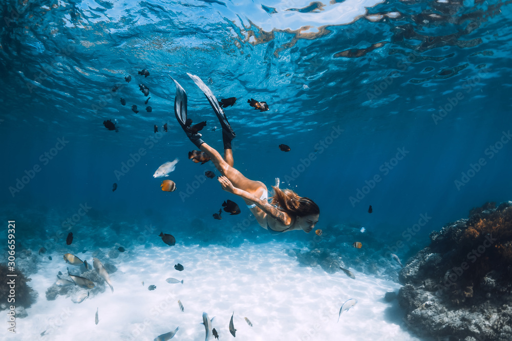 Fototapeta Freediver z płetwami ślizga się po piaszczystym dnie z rybami w błękitnym oceanie