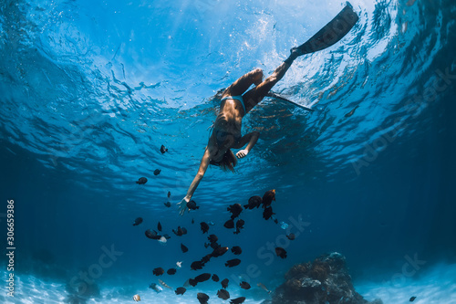 Freediver girl with fins glides over sandy bottom with fishes in blue ocean © artifirsov