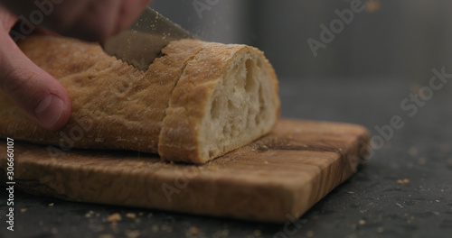 man slicing ciabatta with bread knife on olive board