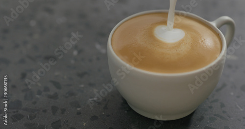 pouring steamed milk into cappuccino in white cup on terrazzo countertop