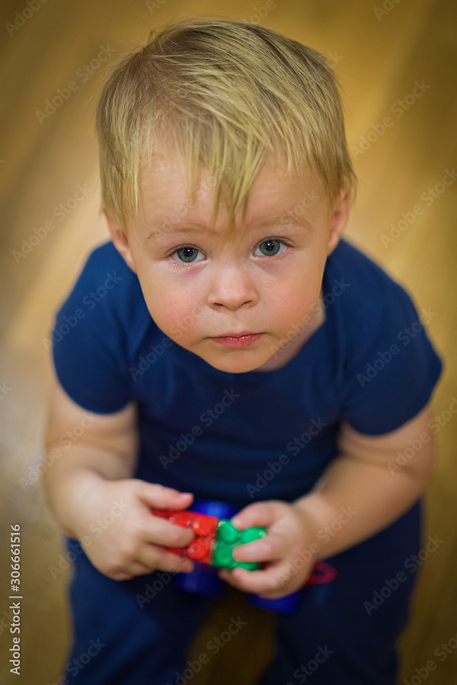 Portrait of a cute little boy with toys in his hands sitting on the floor, looking up. top view