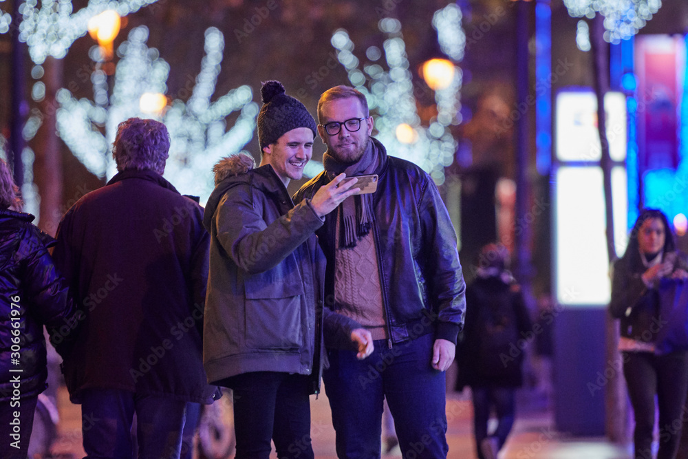 homosexual couple of boys, shopping, at Christmas, at night, they will click on the smartphone the photo they have taken homosexual couple of boys, shopping, at Christmas, at night, they will click on the smartphone the photo they have taken