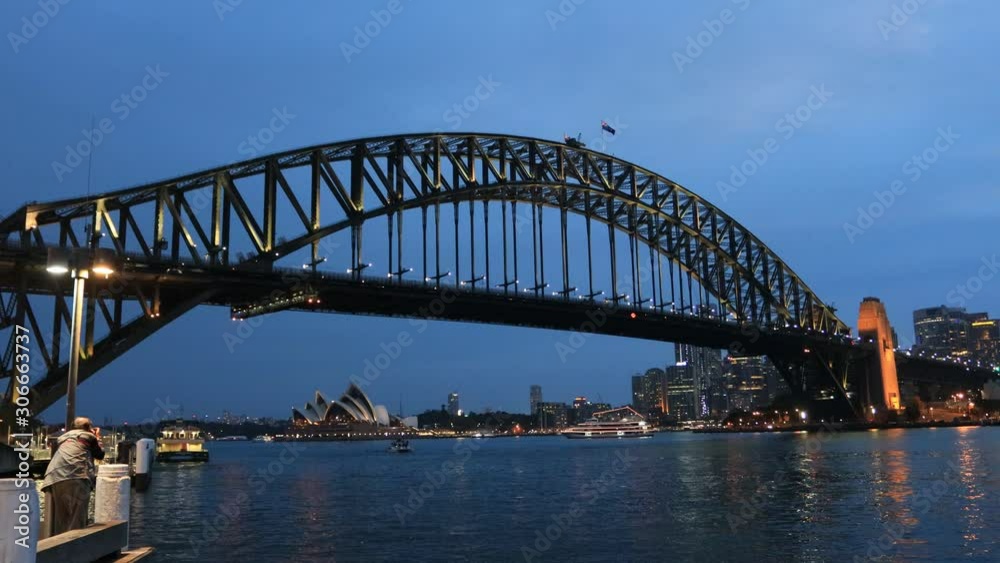 Flags over massive steel arch of the Sydney Harbour bridge at sunset against dark blue sky with bright illumination. Flags over massive steel arch of the Sydney Harbour bridge at sunset against dark blue sky with bright illumination.
