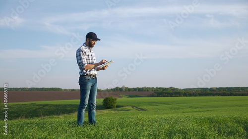 Farmer with a beard and a cap works on the field in spring, use a digital tablet. Farmer using digital tablet. Concept of technologies.