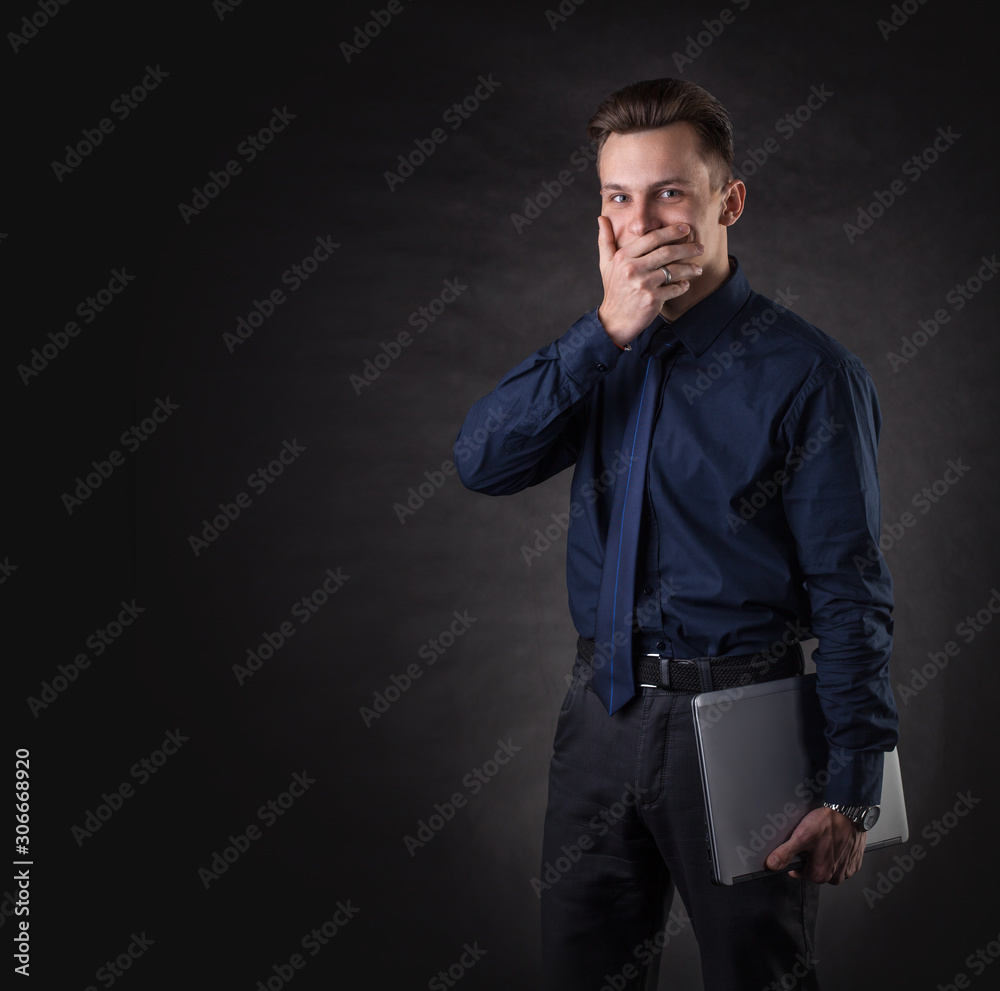 Successful business man on a dark background with a laptop. Sales Manager covers his mouth with his hand Successful business man on a dark background with a laptop. Sales Manager covers his mouth with his hand