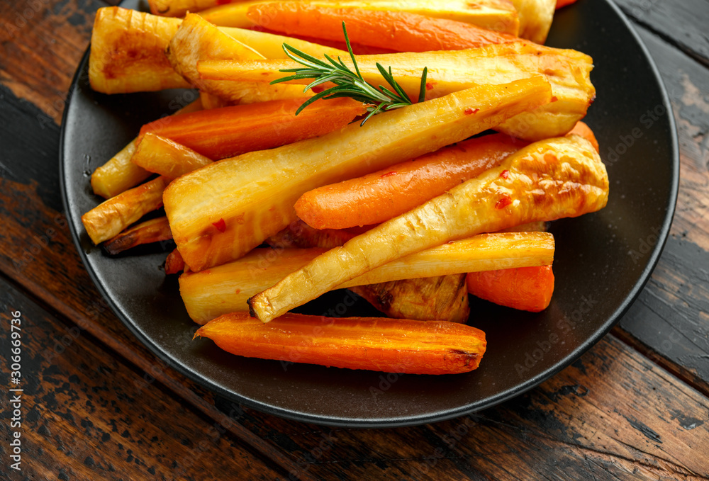 Roasted Parsnips and Carrots with herbs on rustic wooden table Roasted Parsnips and Carrots with herbs on rustic wooden table