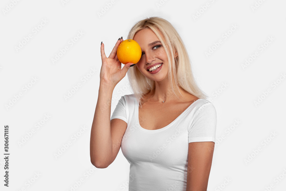 Beauty, sexy blonde girl with perfect healthy hair and natural makeup posing in studio with an orange. Young woman portrait isolated on white background Beauty, sexy blonde girl with perfect healthy hair and natural makeup posing in studio with an orange. Young woman portrait isolated on white background